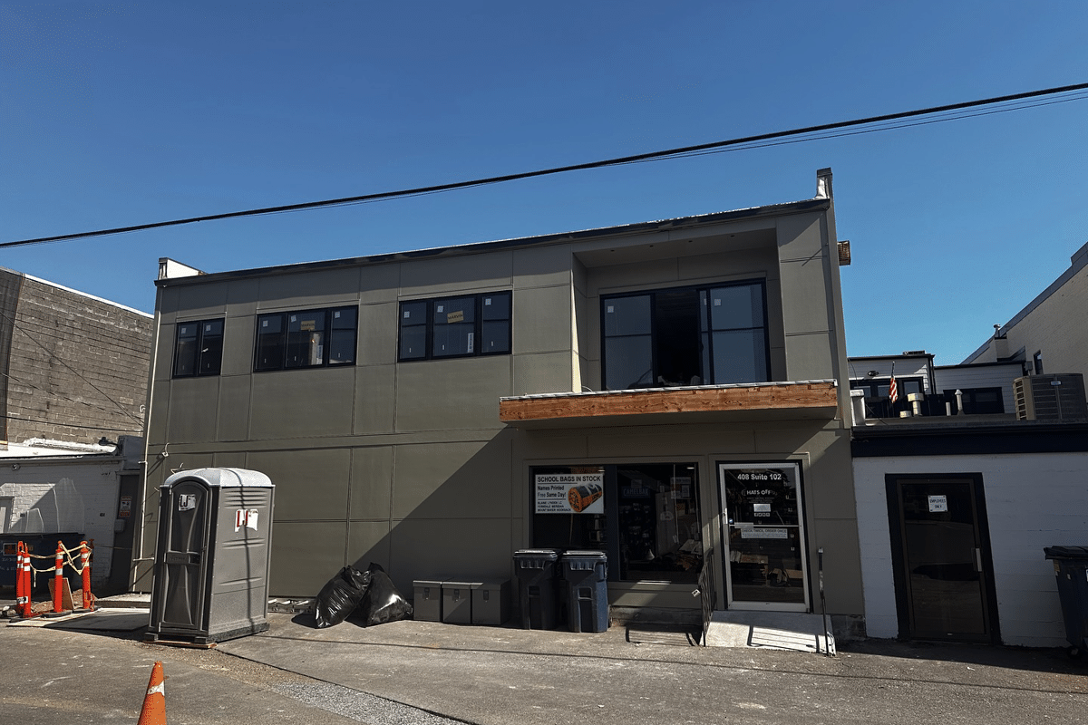 home-service-commercial | Laika Construction | Bellingham Contractor Two-story storefront under renovation with beige panels, large windows, and a portable toilet on the left.