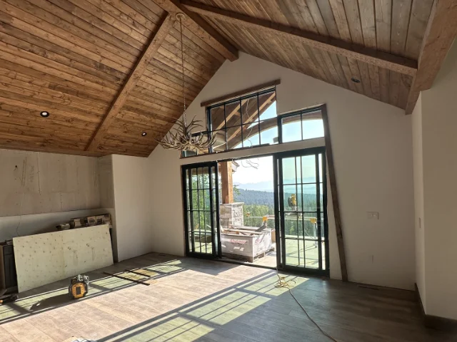 home-service-remodels Living room with a vaulted wooden ceiling and large glass doors opening to a deck; an antler chandelier hangs overhead.