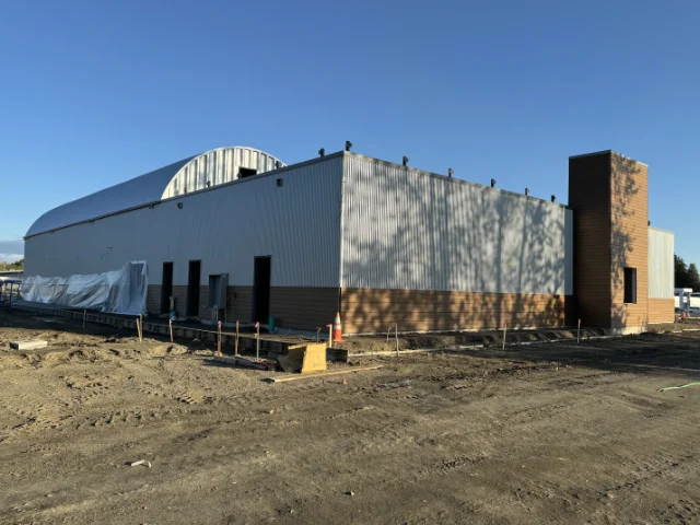 home-service-tenant-improvements | Laika Construction | Bellingham Contractor Industrial warehouse under construction: corrugated metal building with a curved roof section, brick tower, and a dirt lot in the foreground.